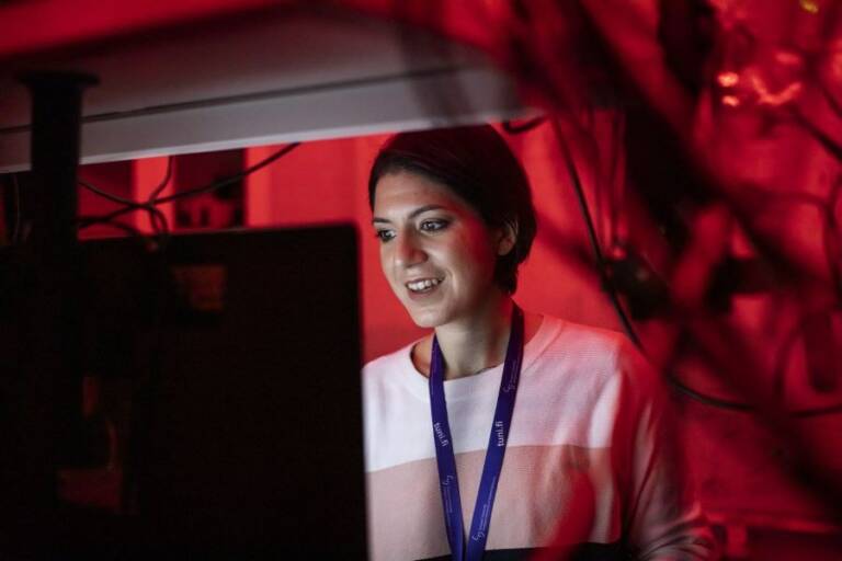Chiara is in dark room in red light looking at the monitor of a microscope.