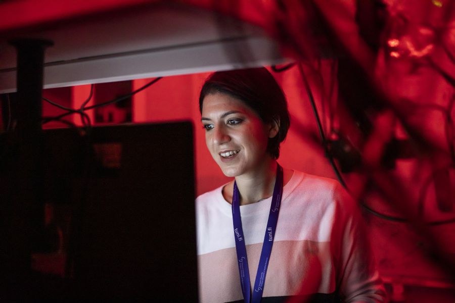 Chiara is in dark room in red light looking at the monitor of a microscope.