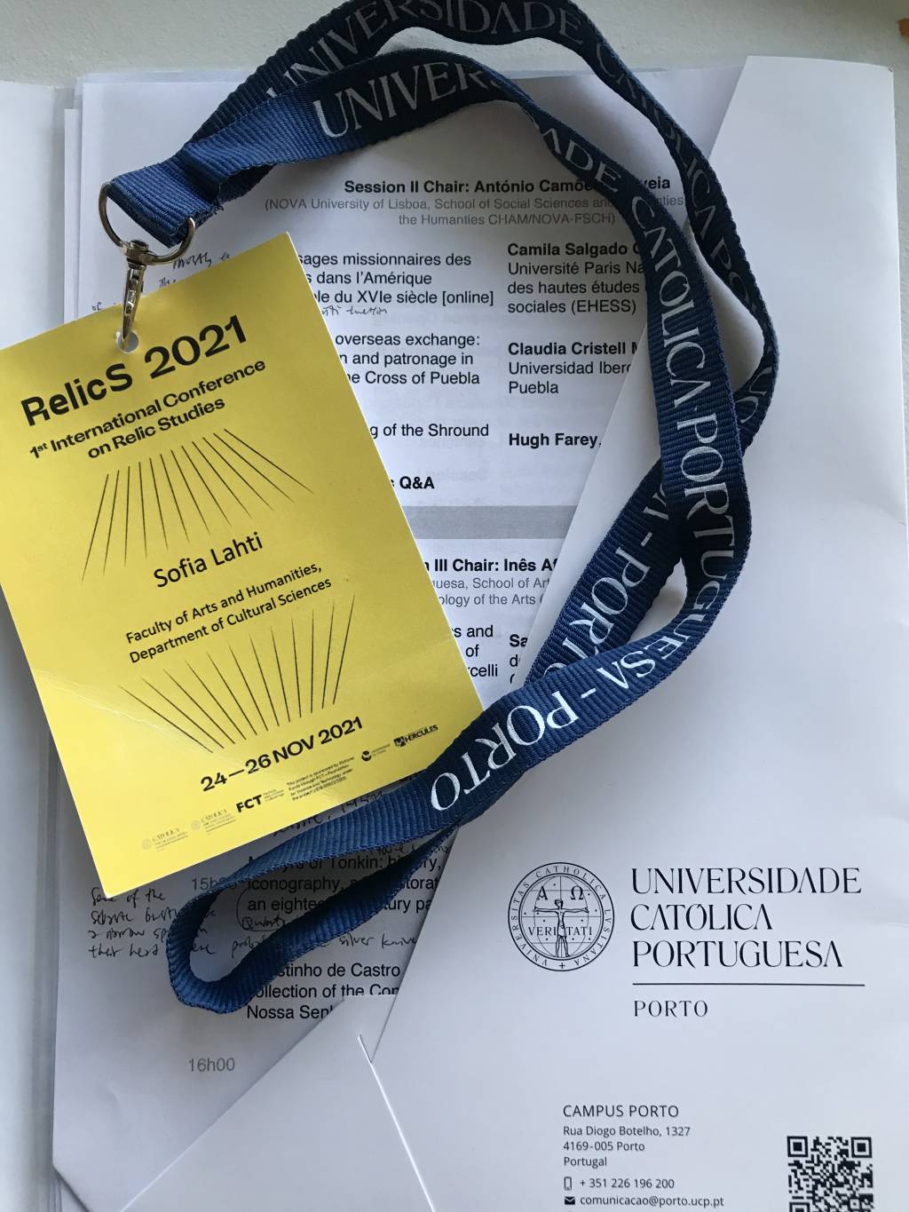 Kuvassa on konferenssiohjelmapapereita ja niiden päällä osallistujan nimikyltti kaulanauhoineen.