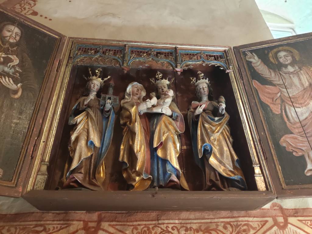 Altarskåpet i Masko kyrka med fyra kvinnliga helgon i guld- och blåfärgade mantlar och klänningar: sankta Gertrud av Nivelles krönt med guldkrona och hållandes en miniatyr av en kyrka. I mitten sankta Anna räckandes ett äpple till Jesusbarnet i den krönta Jungfru Marias famn. Längst till höger står sankta Barbara också hon krönt med en guldkrona och hållandes en bok i handen och en miniatyr av ett torn.