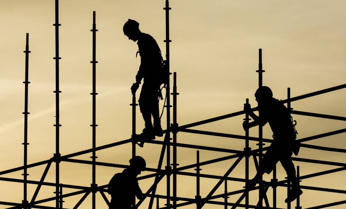 Silhouettes of three people standing and climbing on a construction framework.