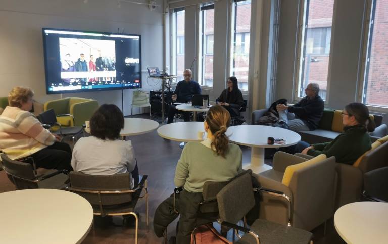 A picture taken at the event, where a group of people are sitting in a circle and following a presentation.