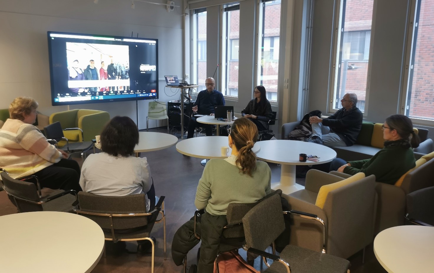 A picture taken at the event, where a group of people are sitting in a circle and following a presentation.