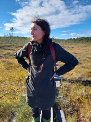 A dark haired woman standing on duckboards on a swamp. swamp