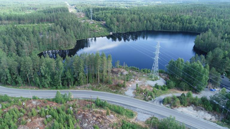 Picture taken from drone up in the air that shows power lines going in the middle of woods and over a lake.