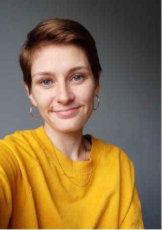 A short-haired woman in a yellow shirt smiles at the camera.