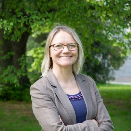 A photo of a blond woman with eyeglasses and a blazer smiling at the camera.