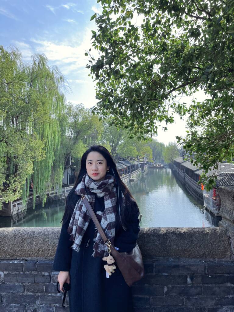 Dr. Jie Jiang outside standing on a bridge over a river.