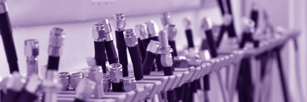 Close up picture of cables with SMA connectors hanging on a rack. Purple hued picture.