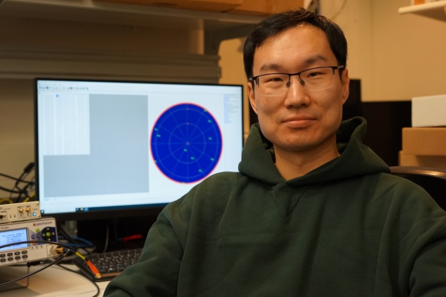Wenbo Wang profile photo, sitting in front of computer that shows GNSS based data.