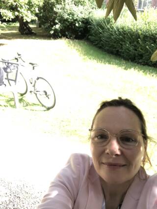 A woman wearing spectacles smiles at camera, bicycles in the background.