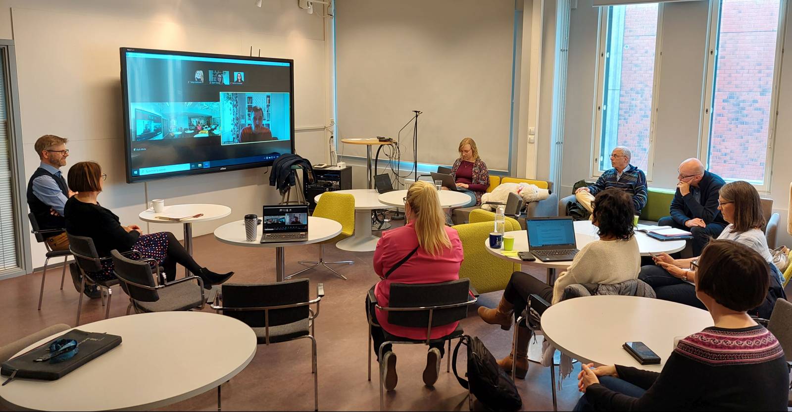 A picture taken at the event, where a group of people are sitting in a circle and following a presentation.