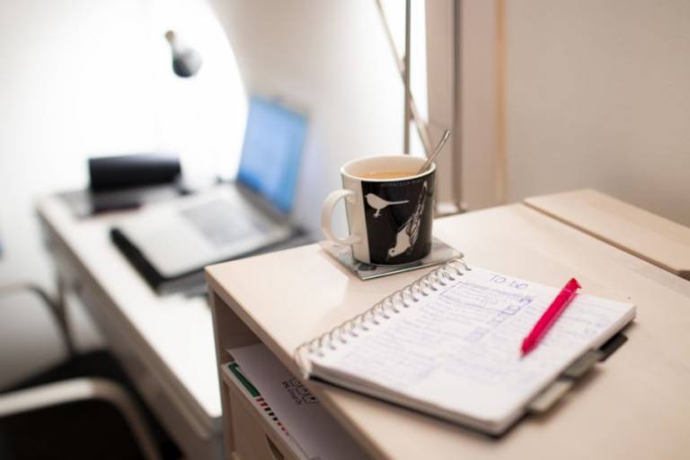 On the background open laptop. In front a coffee mug, notebook and a pen