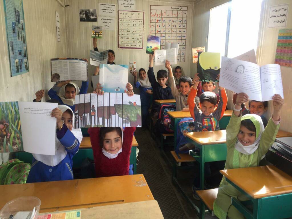 A class room with children showing books.