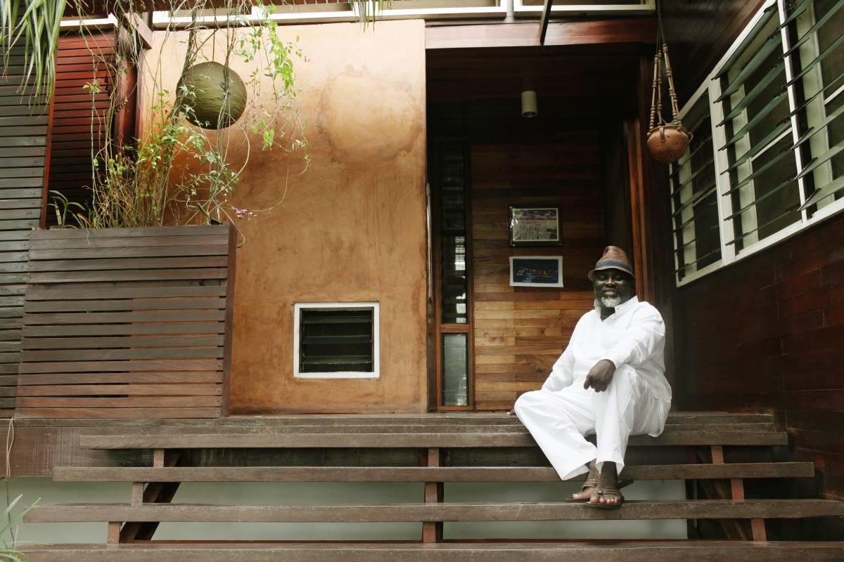 A picture of Joe Osae-Addo, dressed in white, sitting on a porch.
