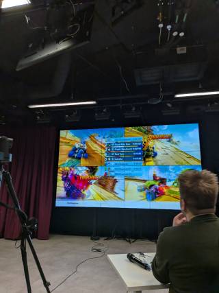 a picture showing the main big screen infront of the venue with four split screen showing small windows of the competitors