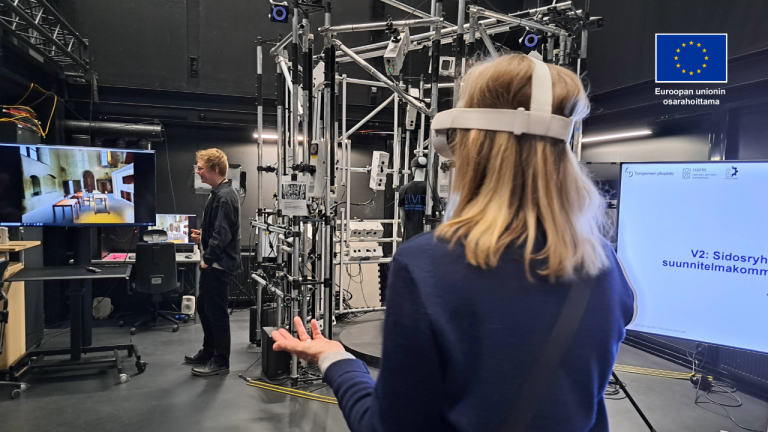 Henkilö XR-lasit päässä. TIlassa on ruutu, jossa näkyy rakennus. Toinen henkilö tarkastelee ruutua.