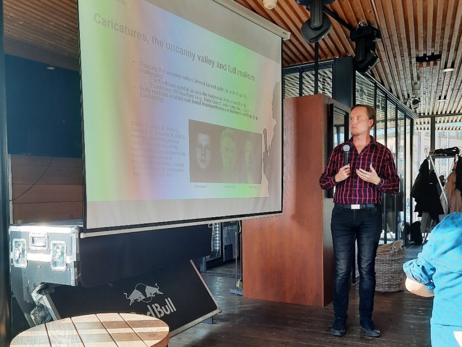 Professor Henri Pirkkalainen giving a presentation. The present slide is titled "Caricatures, the uncanny valley and full realism".