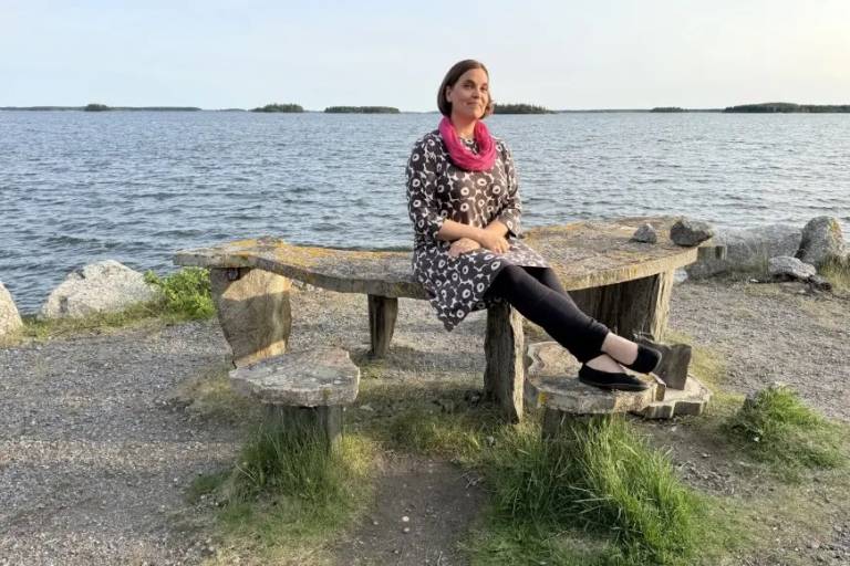 Photo of Heidi Kuusniemi sitting on a beanch on a beach bench.