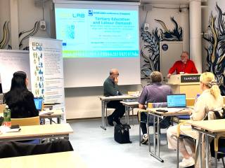 Kuva puheen pitäjästä ja yleisöstä symposiumissa.