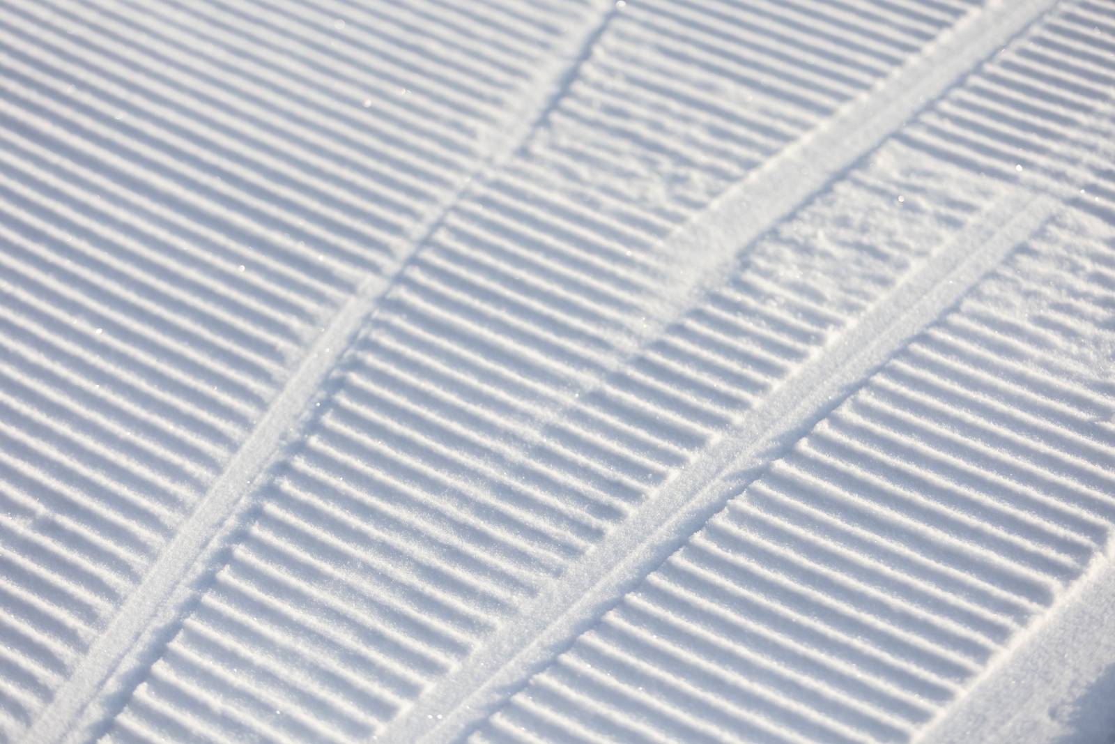 Track lines left behind by skiers going over freshly groomed snow with parallel grooves.