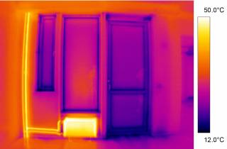 Kuvassa on lämpökameran kuva seinästä, jolla on kaksi ikkunaa, yksi ulko-ovi, ja yksi lämpöpatteri. Kuvan lämpötilaskaala on 12°C-50°C. Oven ja ikkunoiden reunojen lämpötila on lähes 12°C, kun taas patterin lämpötila on noin 50°C. Seinän lämpötila on sillä välillä.