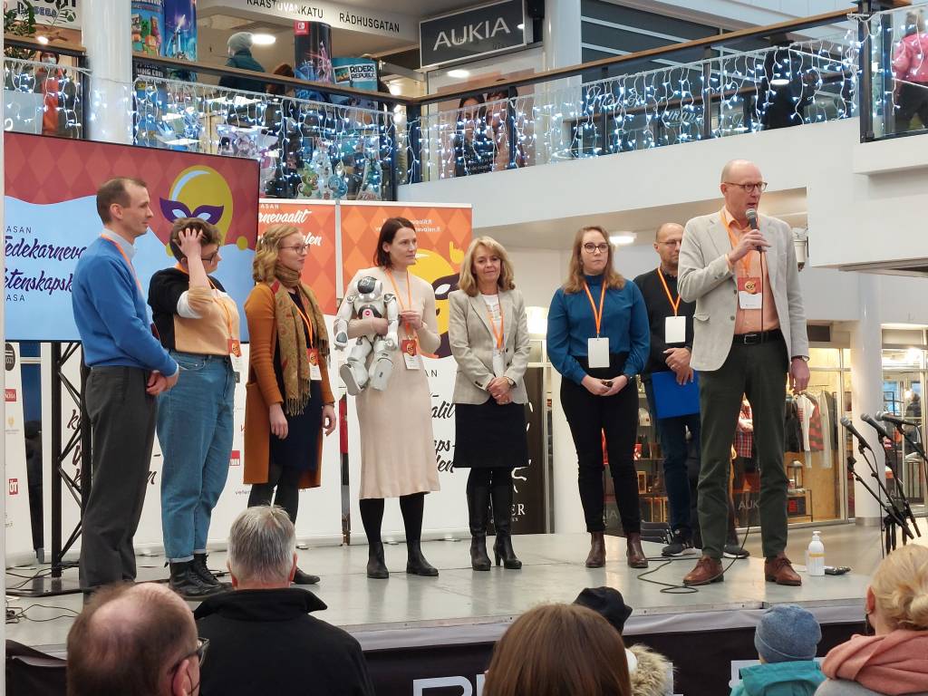 Deltagarna i Science Slam-tävlingen tillsammans med Svenska Litteratursällskapets direktör Christer Kuvaja och tävlingens konferencier Hippi Hovi på scenen i Rewell köpcentrum.