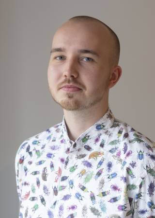 A shorthaired man wearing a colourful bugpatterned shirt.