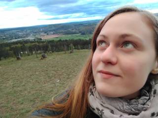 A young woman looking up. In the backround there are hills and trees.