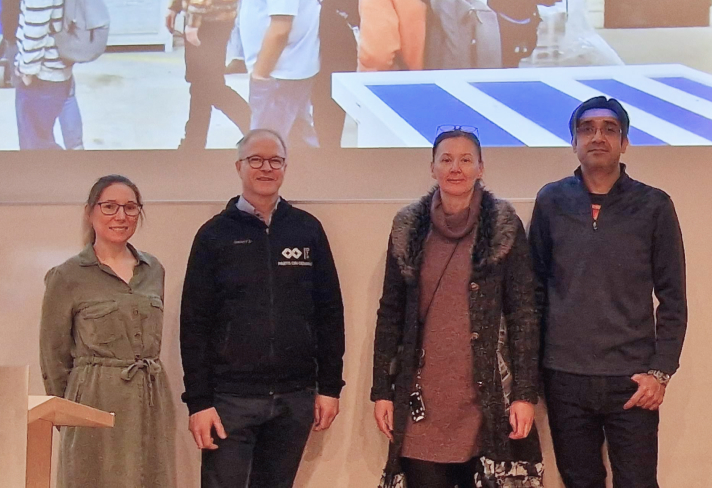 Four people pose in front of a projector image