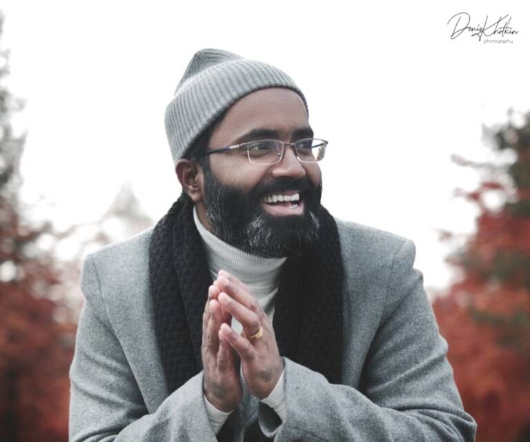 Smiling Rijeesh outside in a coat and a hat in an autumn background